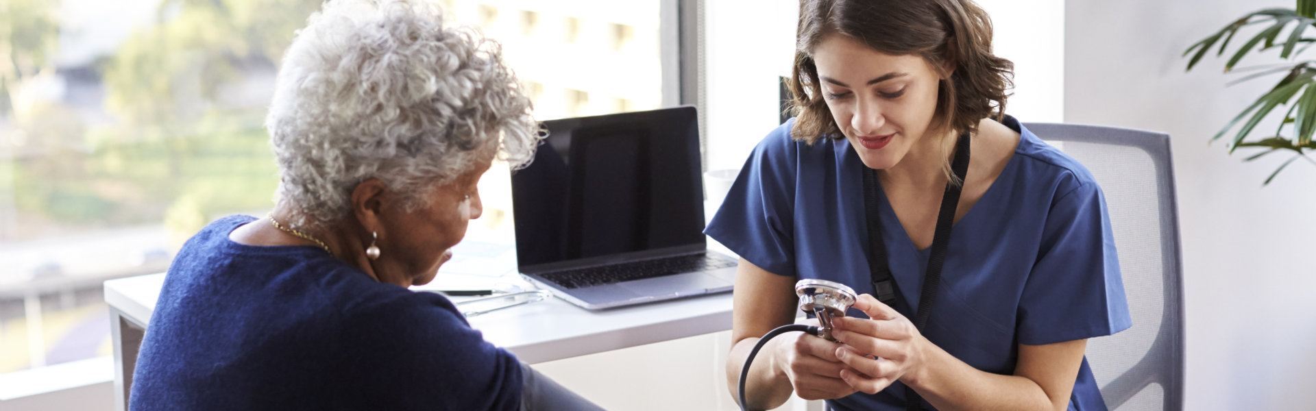 caregiver wearing scrubs In office checking elderly